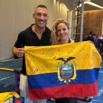 Lourdes, fundadora de Red Lulu Hair Design, junto a Romeo Felipe (embajador global de Wella) con la bandera de Ecuador en el evento Wella Angel, Tulum 2025