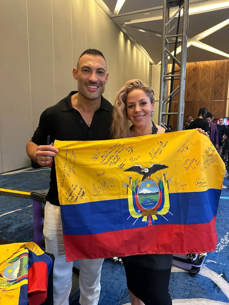 Lourdes, directora artística de Red Lulu, con Romeu Felipe, embajador global de Wella, en el backstage del Wella Beauty Festival 2025 en Tulum, sosteniendo la bandera de Ecuador firmada por los coloristas del evento